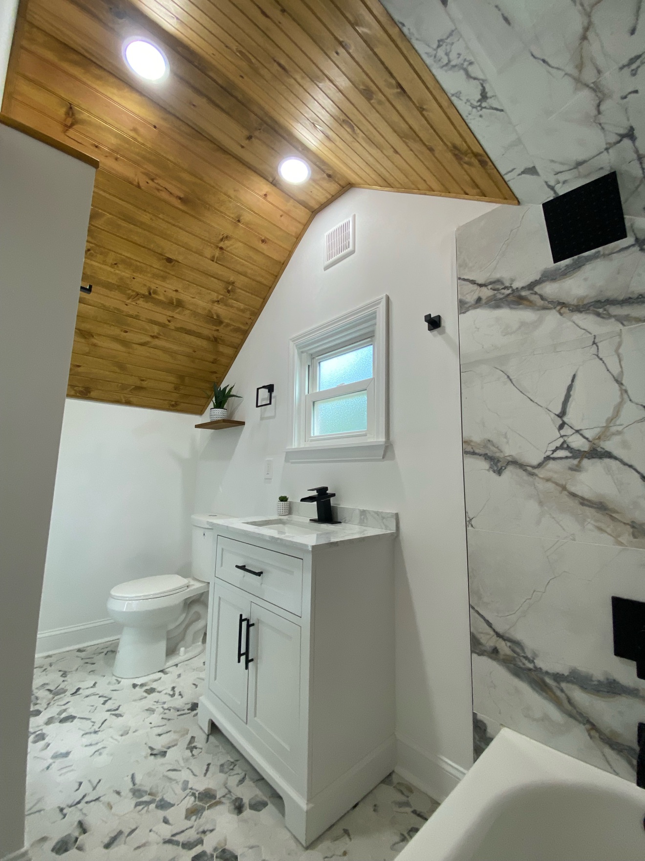 The same finished bathroom from the vanity side — wood-plank ceiling, marble-look tile and stone-pattern hex floor