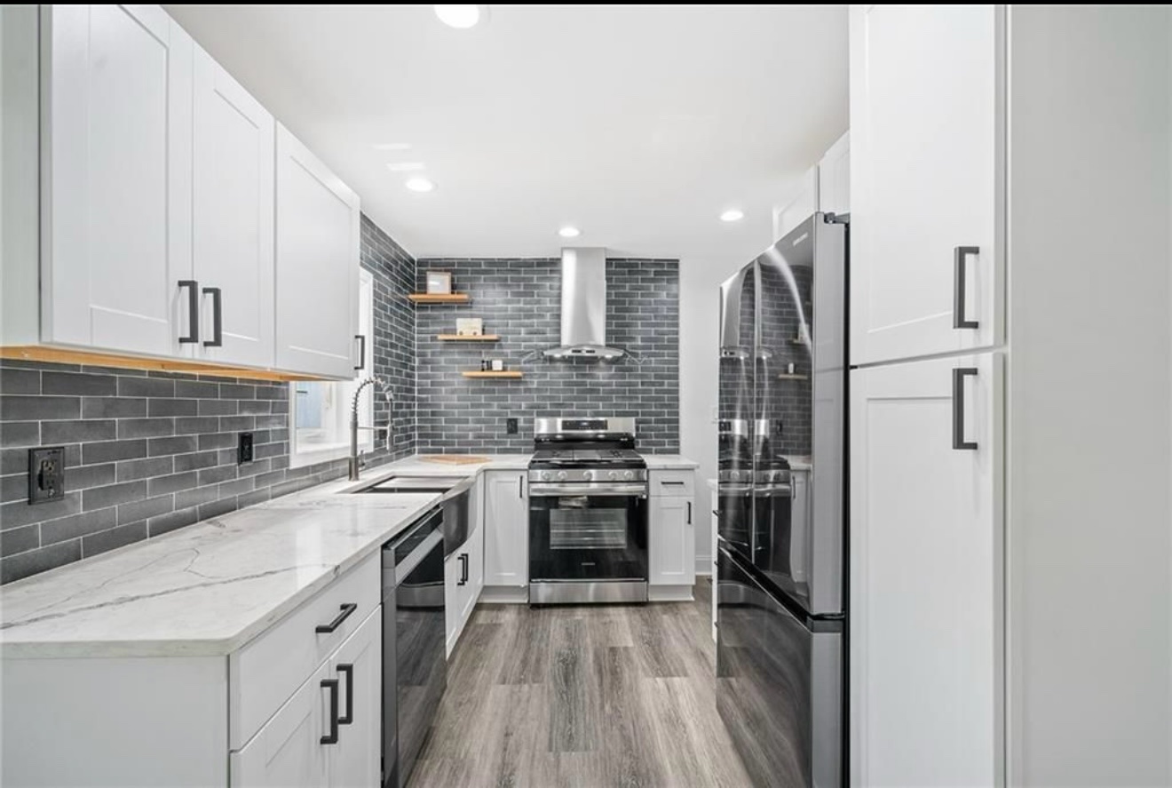 Kitchen with white cabinets, dark gray tile backsplash, marble-look counters and stainless appliances